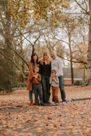 Group portrait on ground covered in fall foliage with trees in background during autumn photo session.