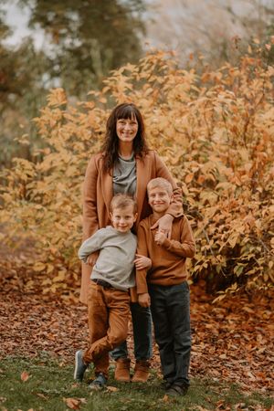 Three people stand together among golden autumn leaves and foliage outdoors.