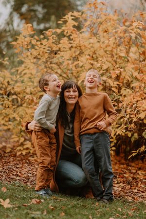 Candid moment of family laughing together amongst golden autumn leaves outdoors.