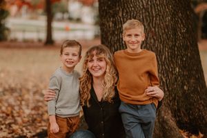 Heartwarming portrait of family leaning against large tree trunk with autumn foliage in background.