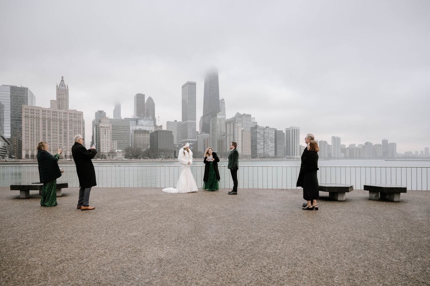 People walk along North Avenue Beach in Chicago with the city skyline visible through thick foggy conditions.