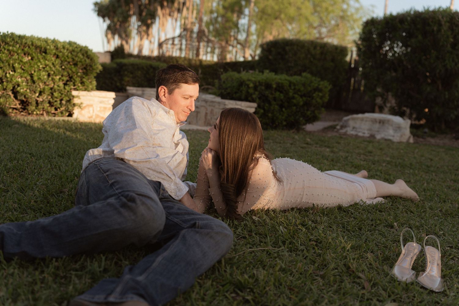Couple relaxing on grass during golden hour outdoor photography session.