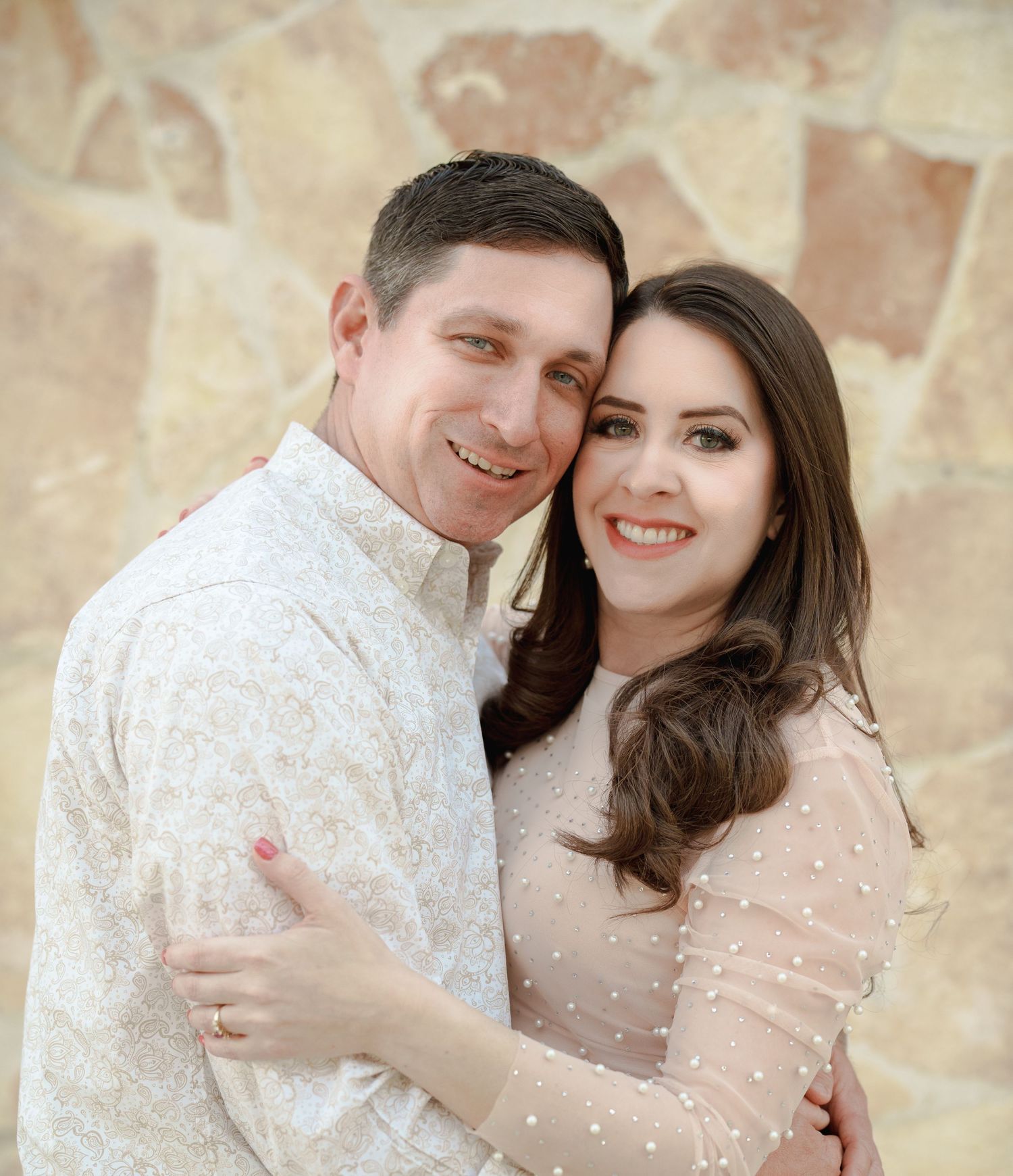 Engagement photos of couple in white clothing posing against stone wall backdrop.