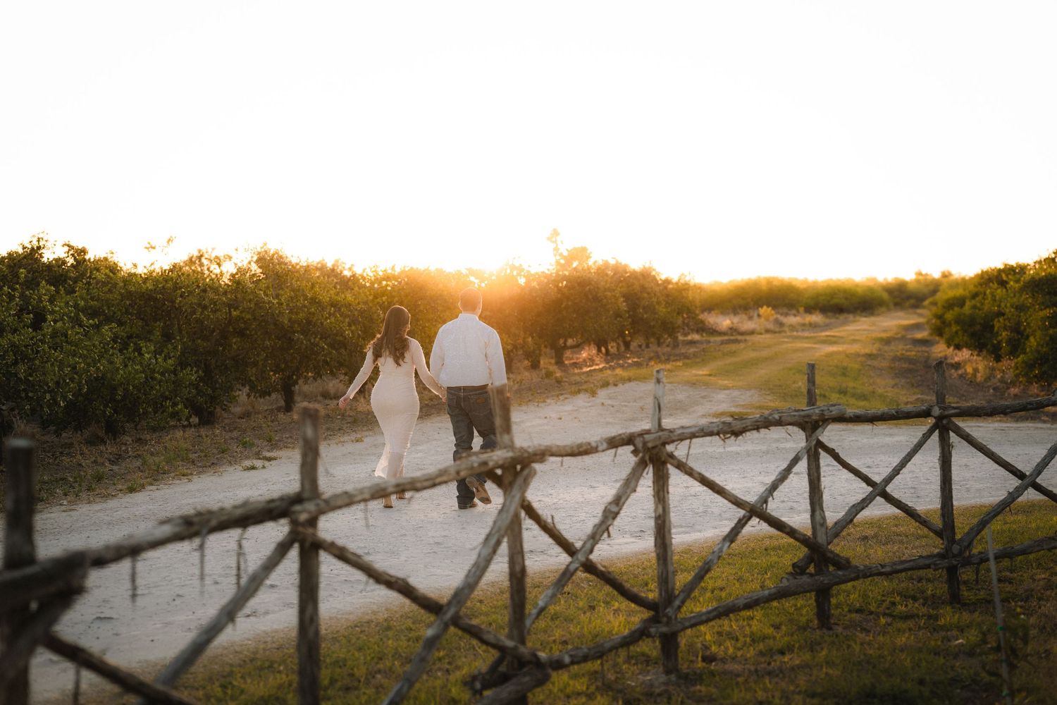 Silhouetted couple walking along wooden fence during sunset engagement session.