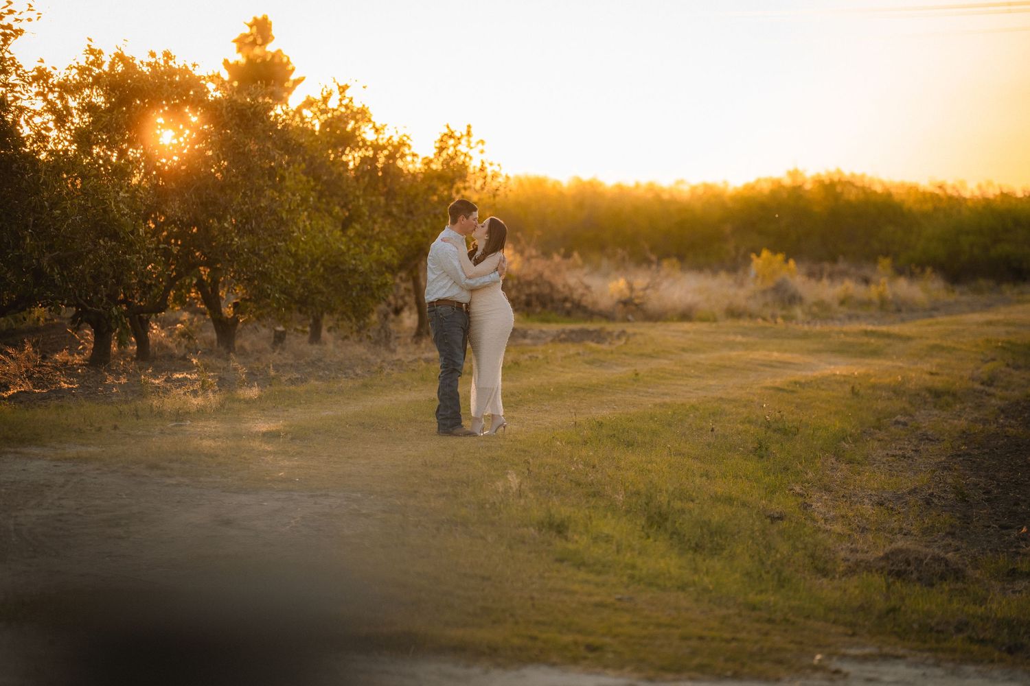 Romantic couple embraces during golden hour sunset in a grassy field with warm lighting.