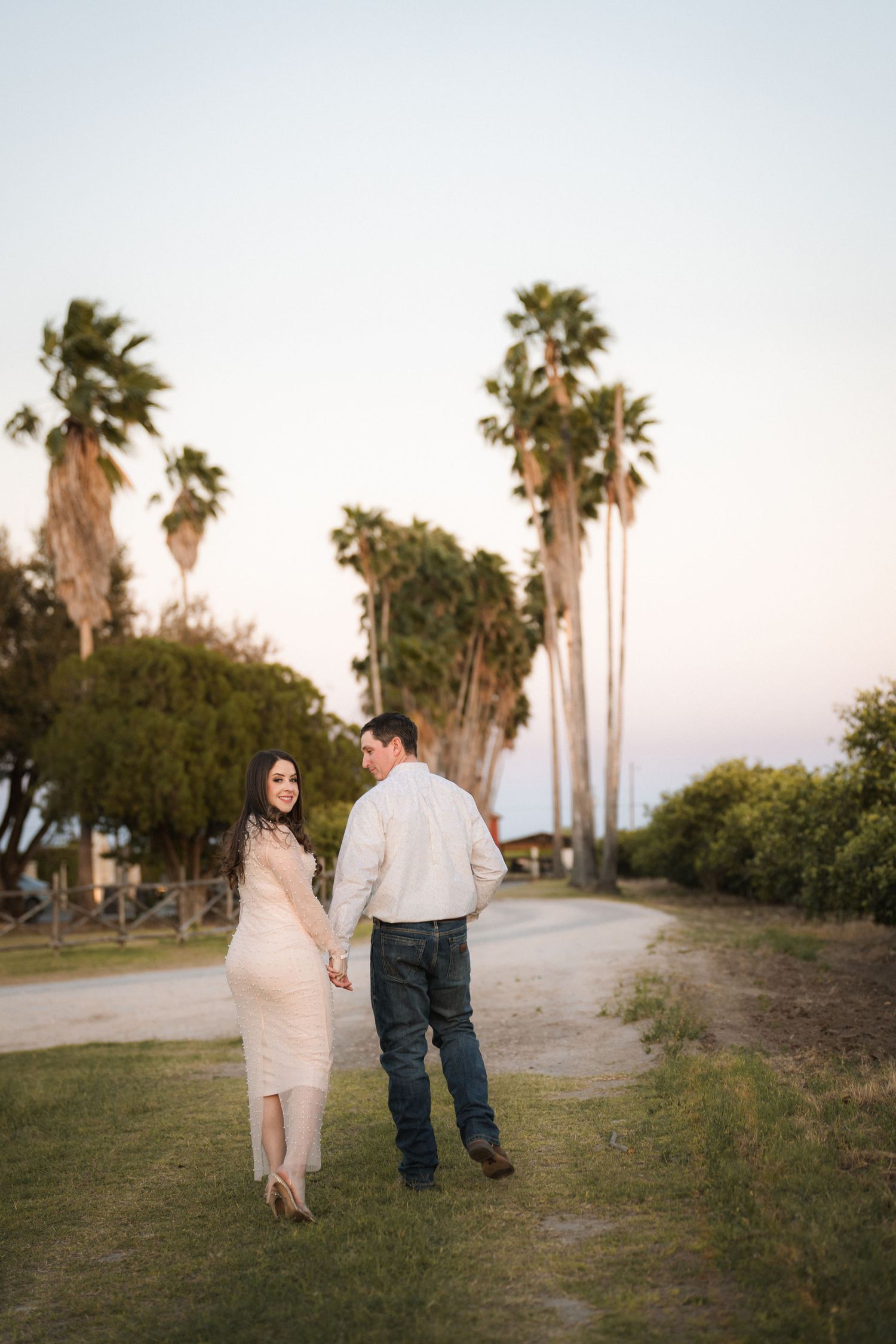 Couple walking along palm tree-lined path during sunset engagement session.