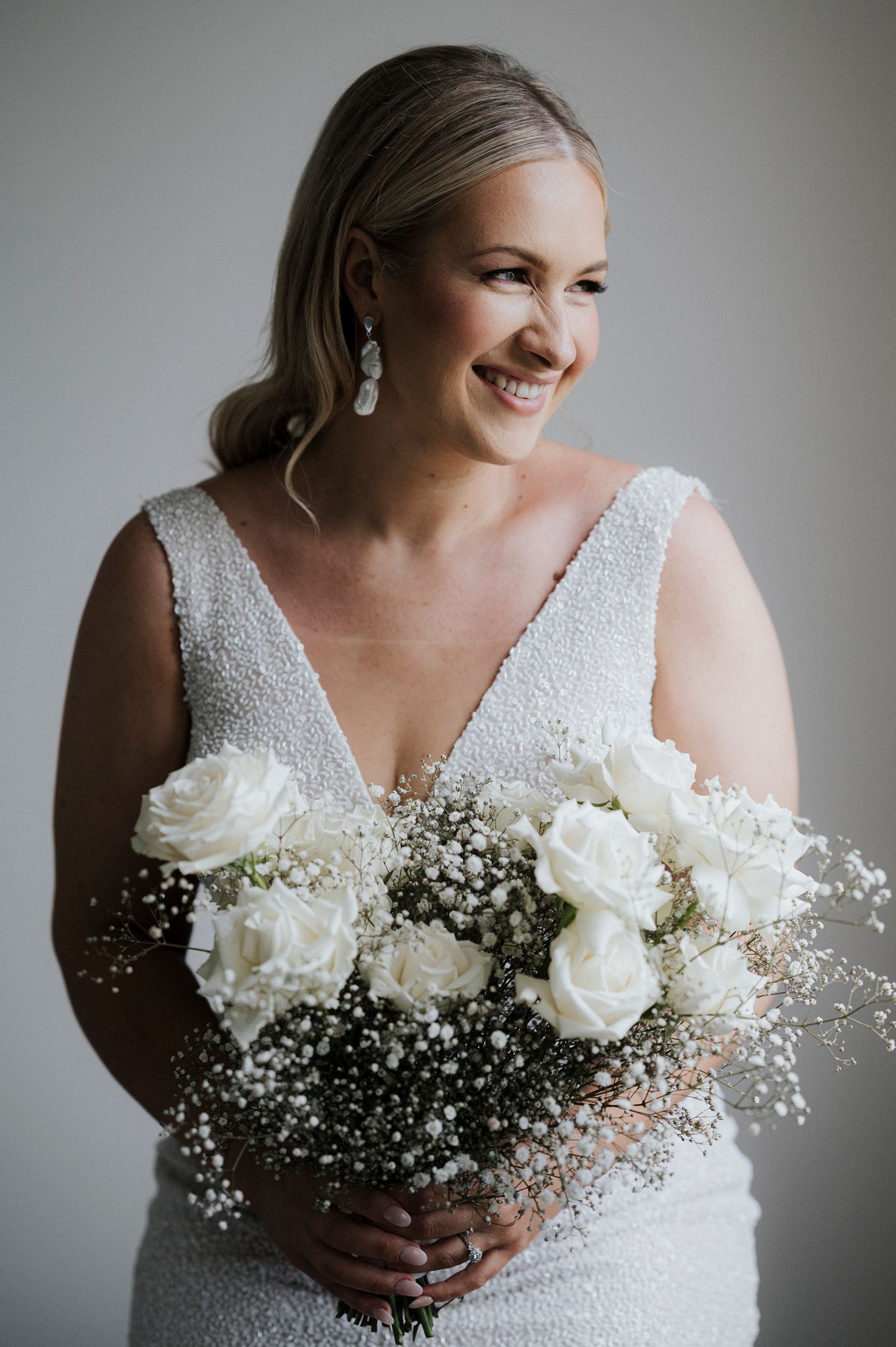 Close-up shots of bridal bouquet with white roses and baby's breath against beaded wedding dress.