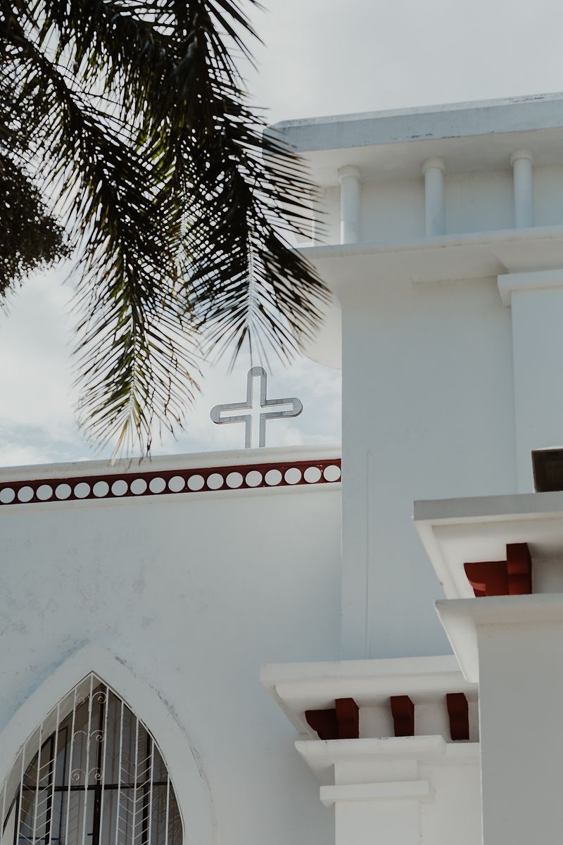 White church exterior with palm fronds and architectural details including a cross symbol and arched window.