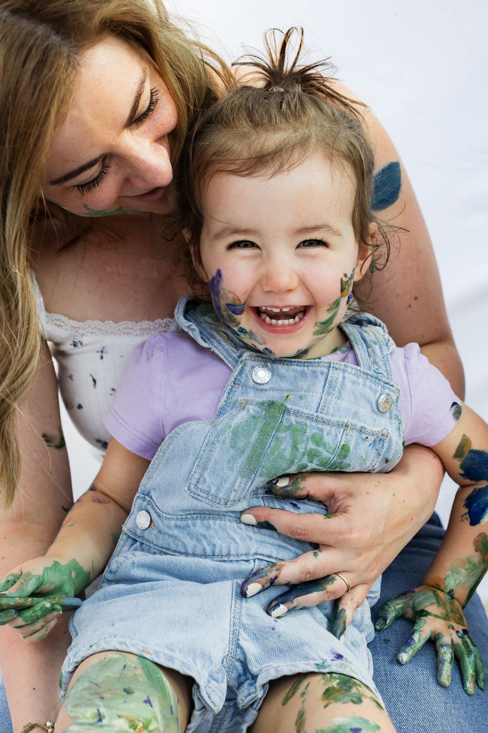 Joyful paint play session with toddler in denim overalls getting messy with green paint.