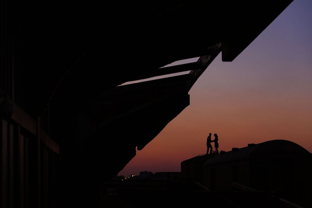 Silhouetted figures stand against a vibrant sunset sky with orange and purple hues.