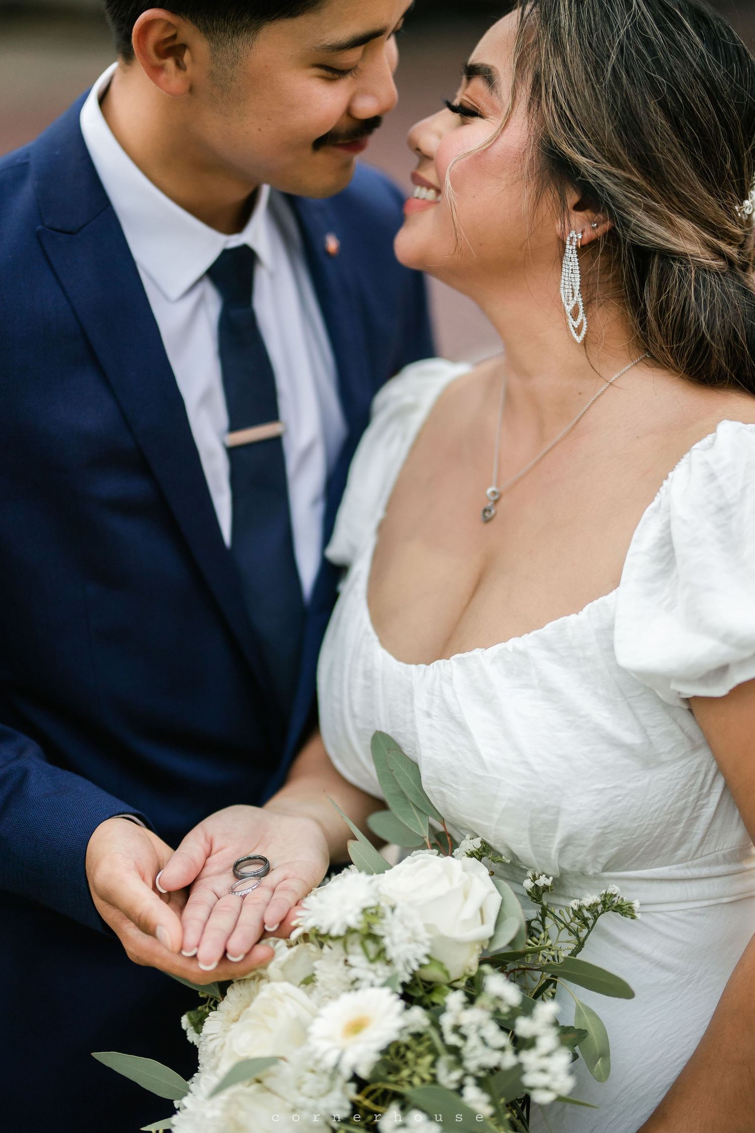 Intimate wedding portrait featuring a smiling couple in navy and white, holding hands with a white floral bouquet.