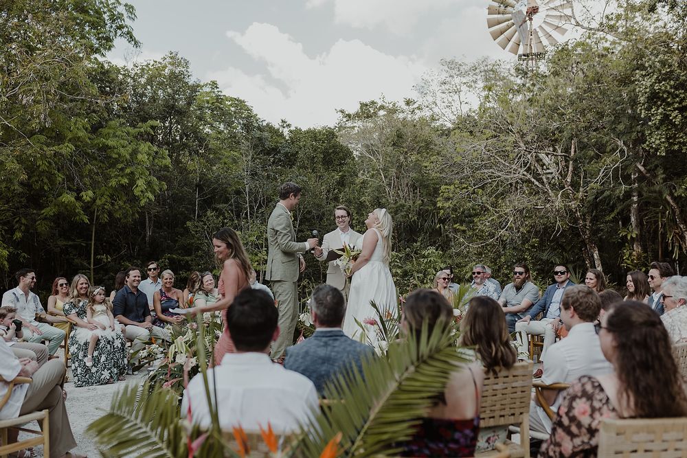 Outdoor wedding ceremony in a tropical forest setting with guests seated around the couple exchanging vows.
