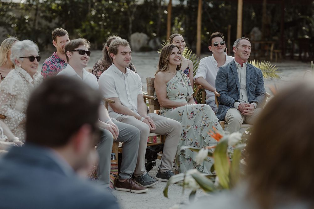 Guests seated outdoors at a wedding ceremony, smiling and watching the event in a tropical garden setting.