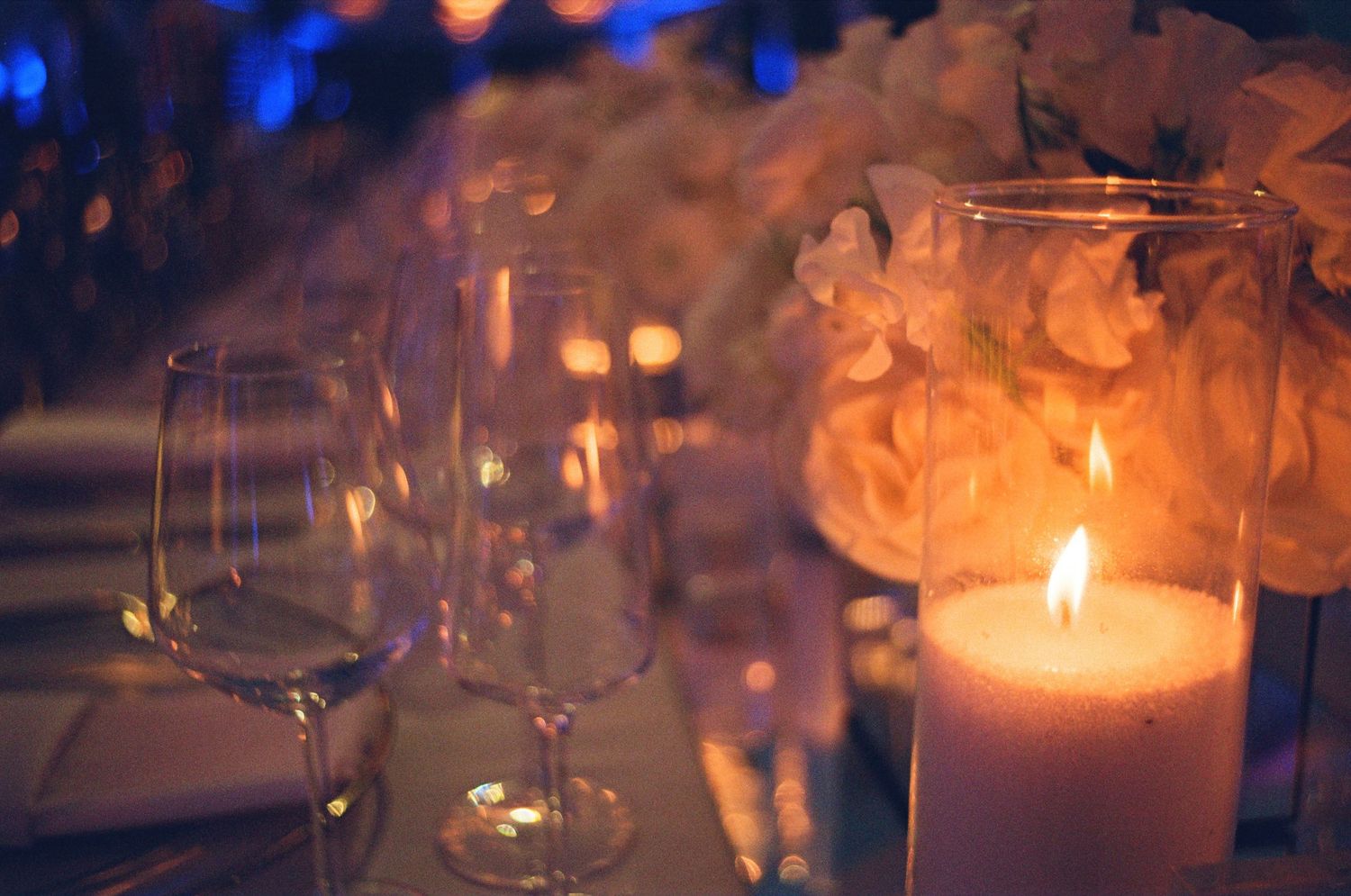 Outdoor elegant wedding table settings with white decor, linens, and glass candle holders against a beachy backdrop.