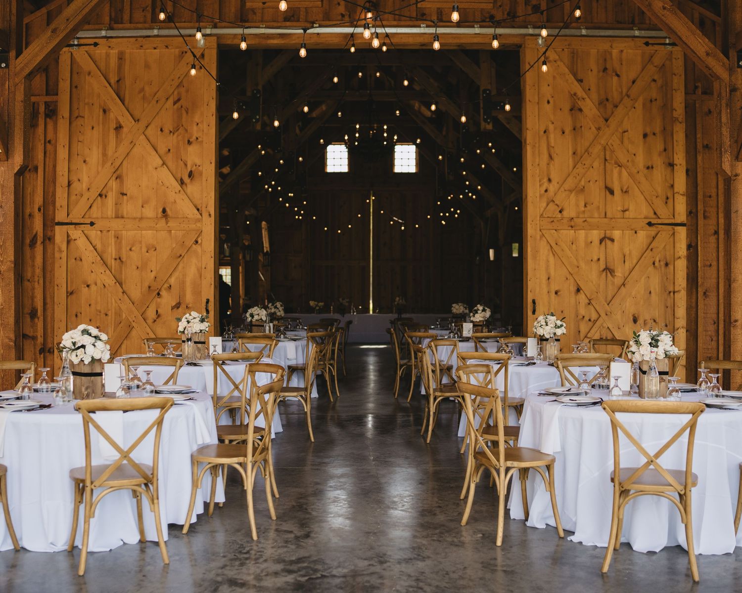 Elegant barn wedding reception with white tablecloths, wooden chairs, and string lights.cinematic wedding photographer new mexico