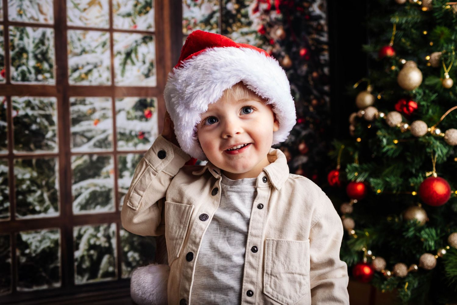 A child wearing a Santa hat looks joyfully at a decorated Christmas tree through a frosty window. Christmas mini shoot, Southport