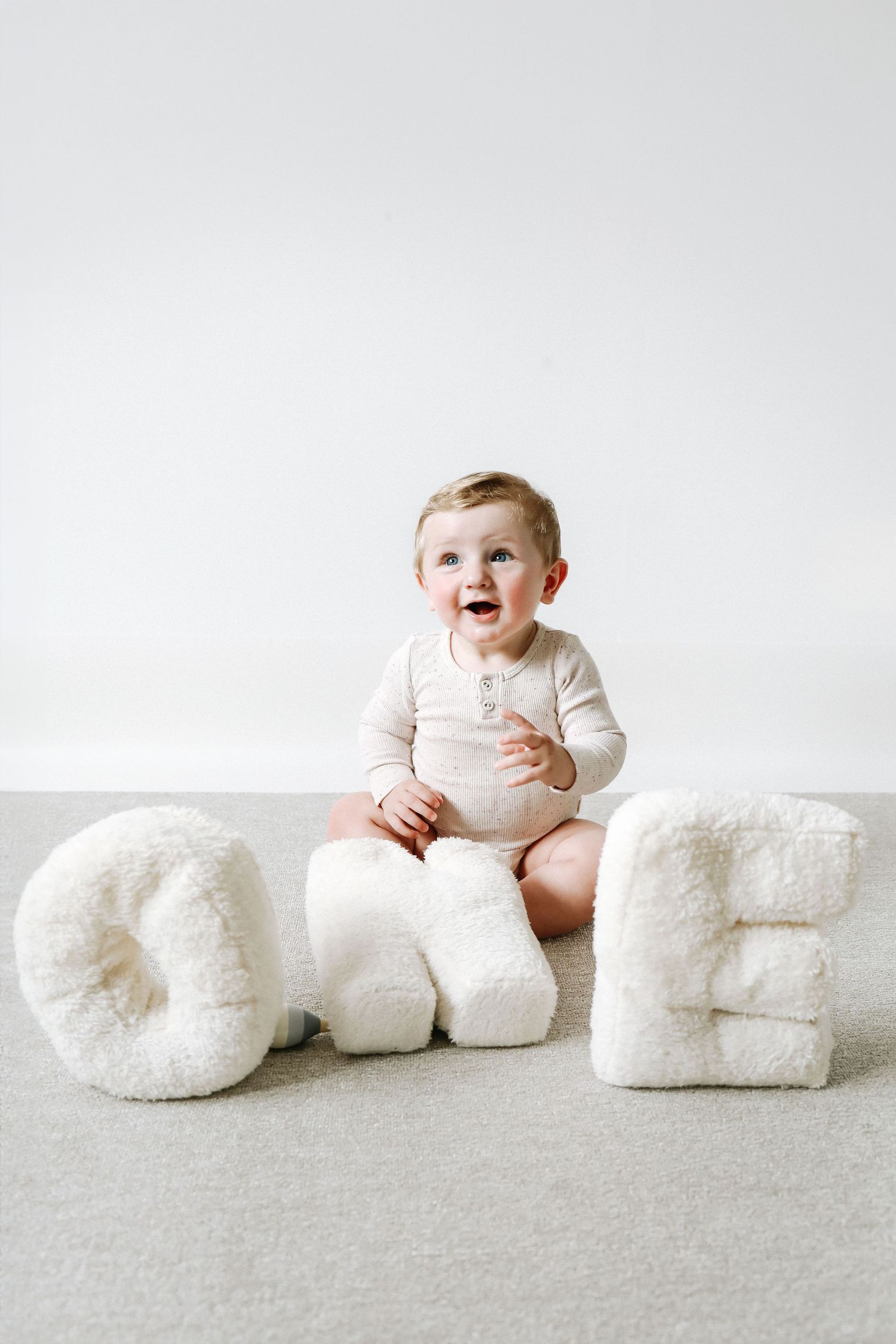 Baby in white onesie sits among white "One" letters during birthday shoot in Nottingham