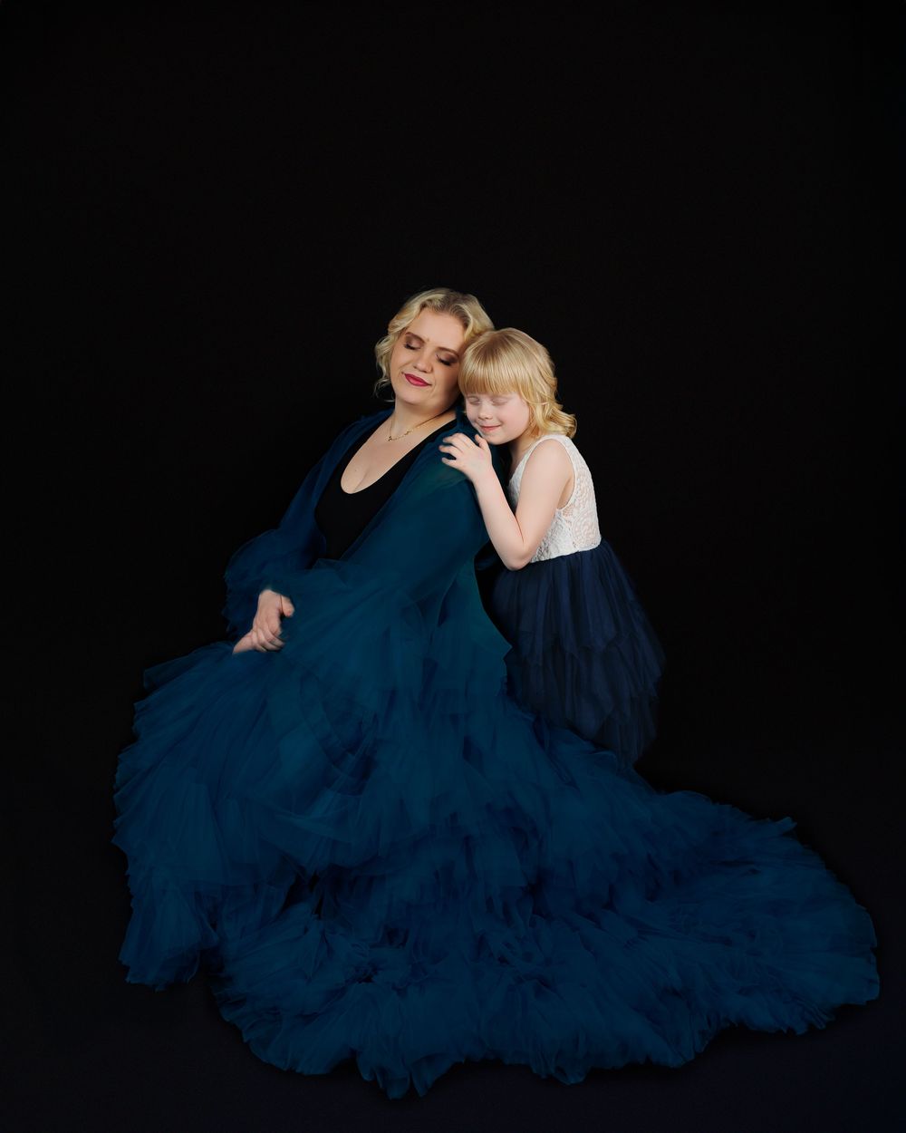 Woman in flowing navy blue tulle dress poses gracefully against black backdrop in artistic portrait series.