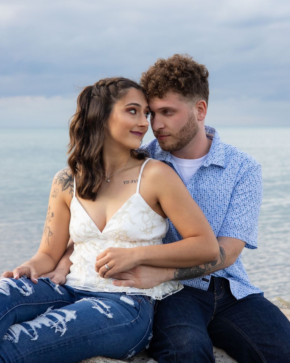 A couple embraces intimately on the beach with the ocean and cloudy sky in the background.