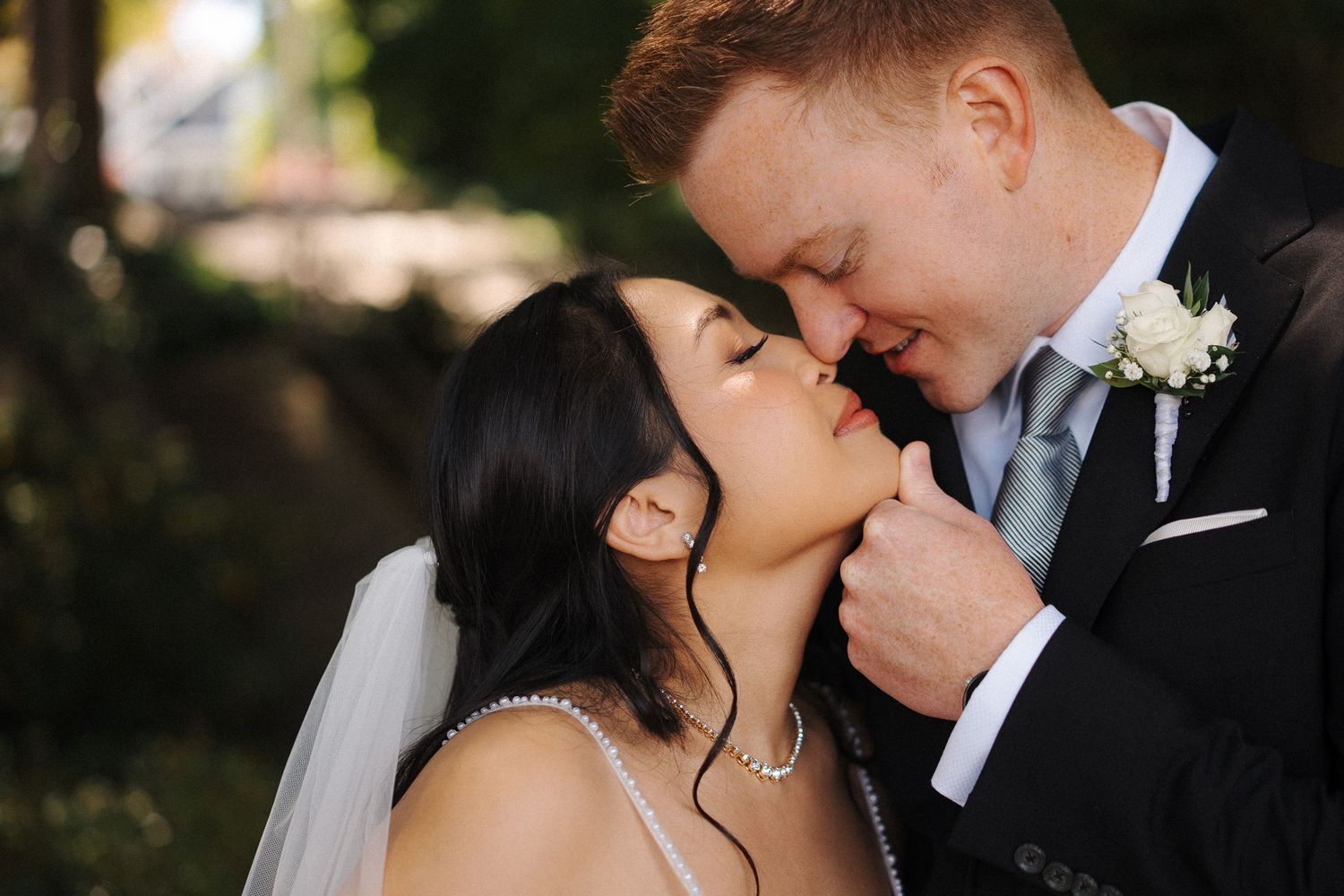 A romantic wedding photo captures an intimate moment between newlyweds in formal attire outdoors.