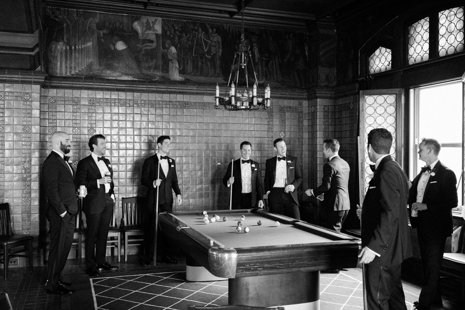 Vintage black and white photo of groomsmen gathered around billiards table in formal attire.