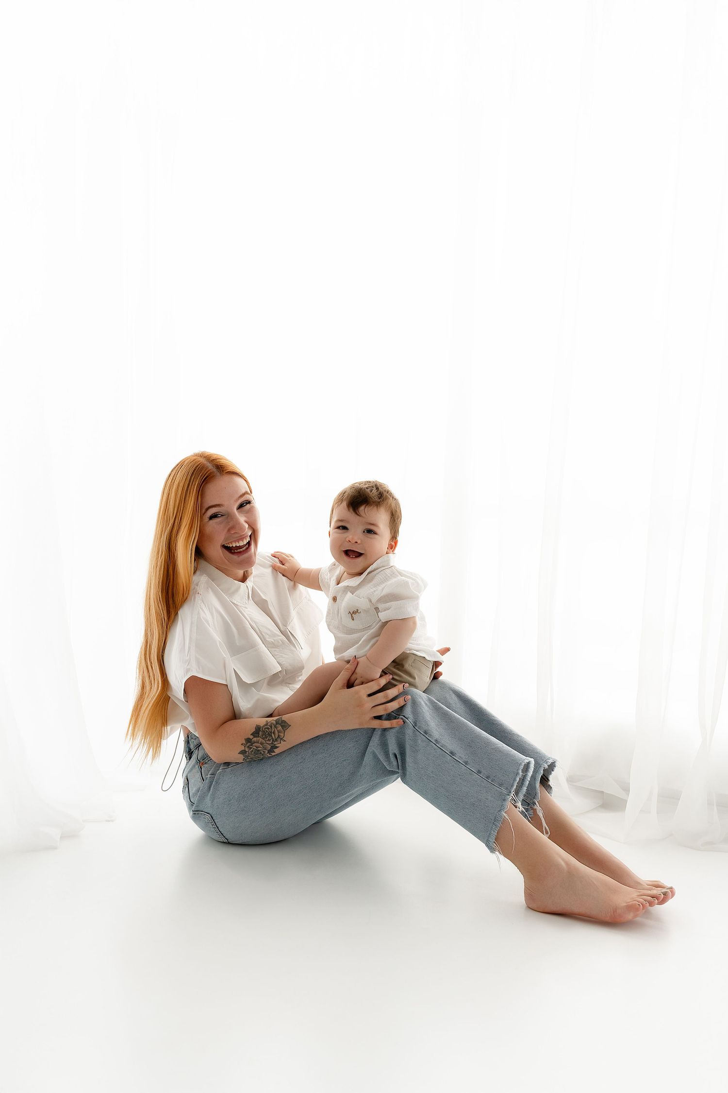 A joyful parent and child share a playful moment together while sitting on a white floor.