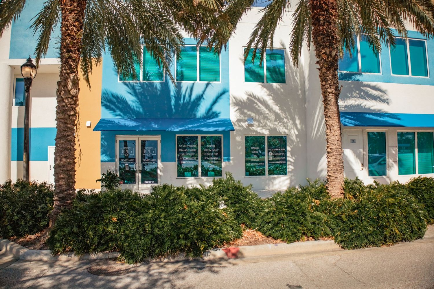 Palm tree lined exterior of a commercial building with white facade and glass windows.