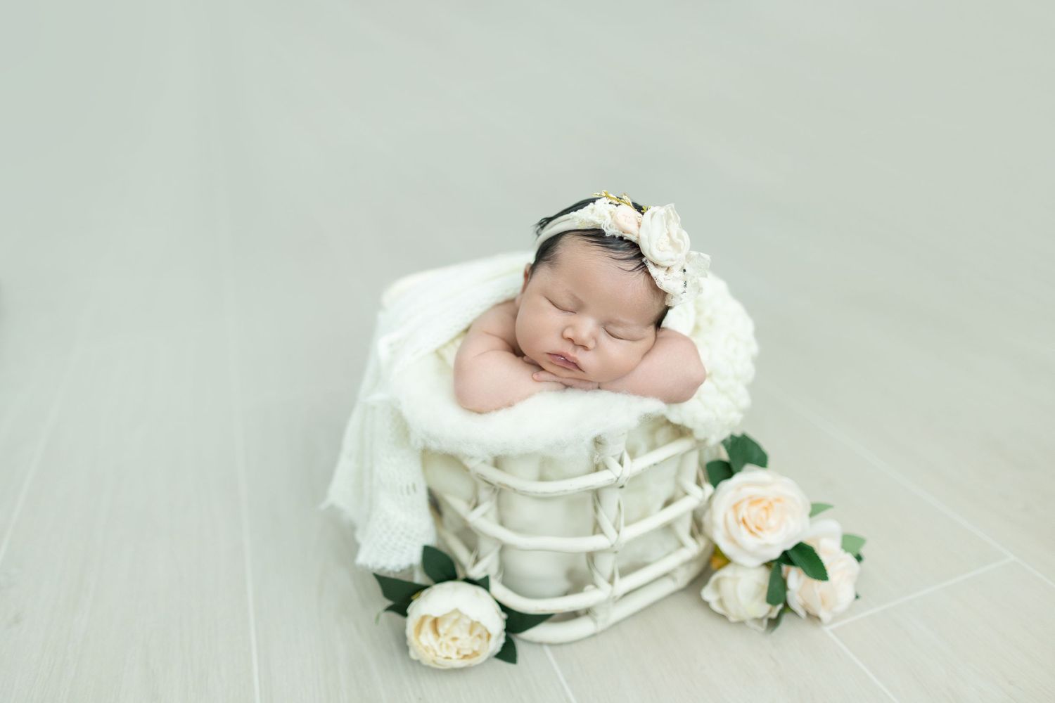 Peaceful sleeping newborn in white wrap with roses during professional studio photoshoot.