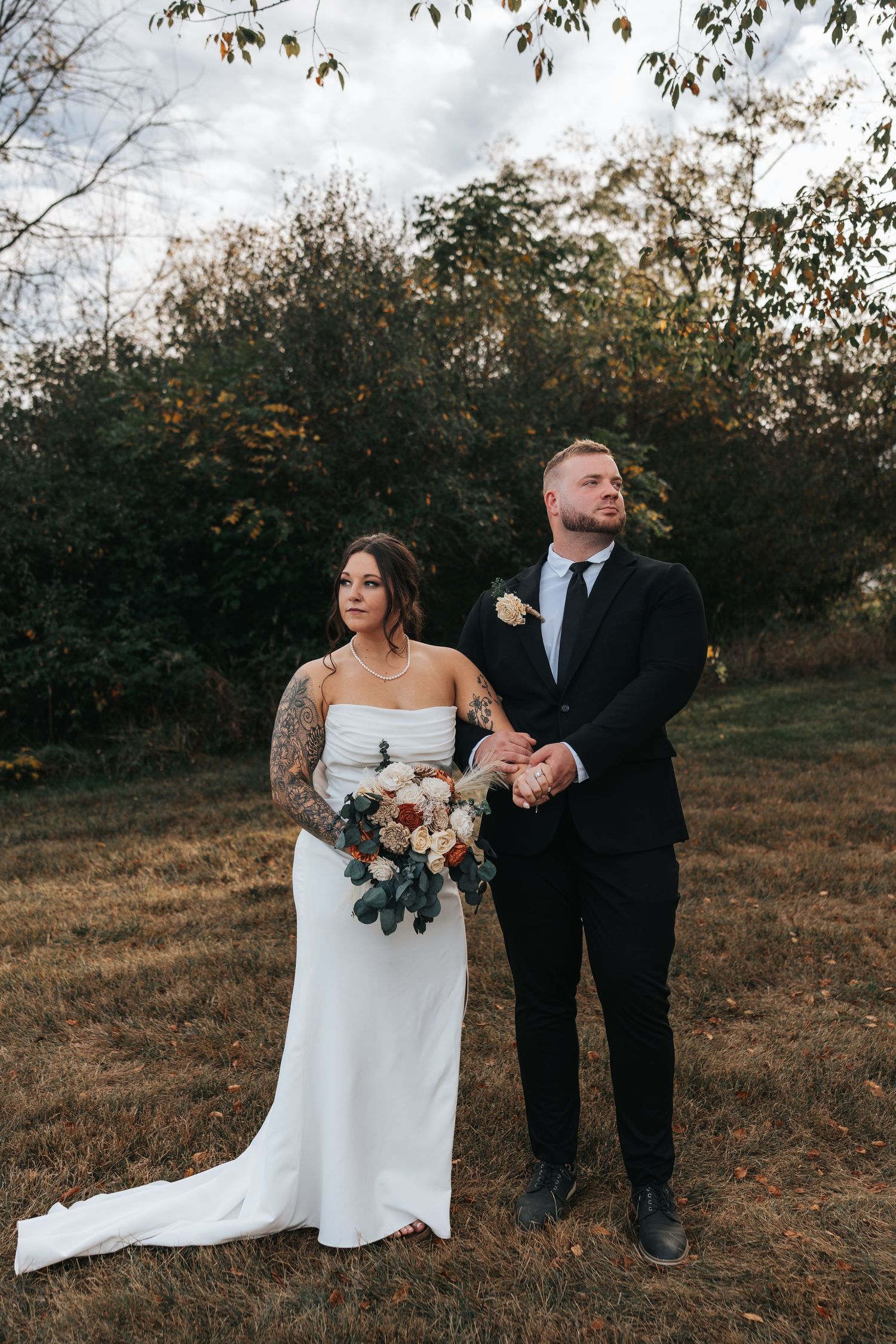 Elegant wedding couple poses in rustic outdoor setting at dusk.