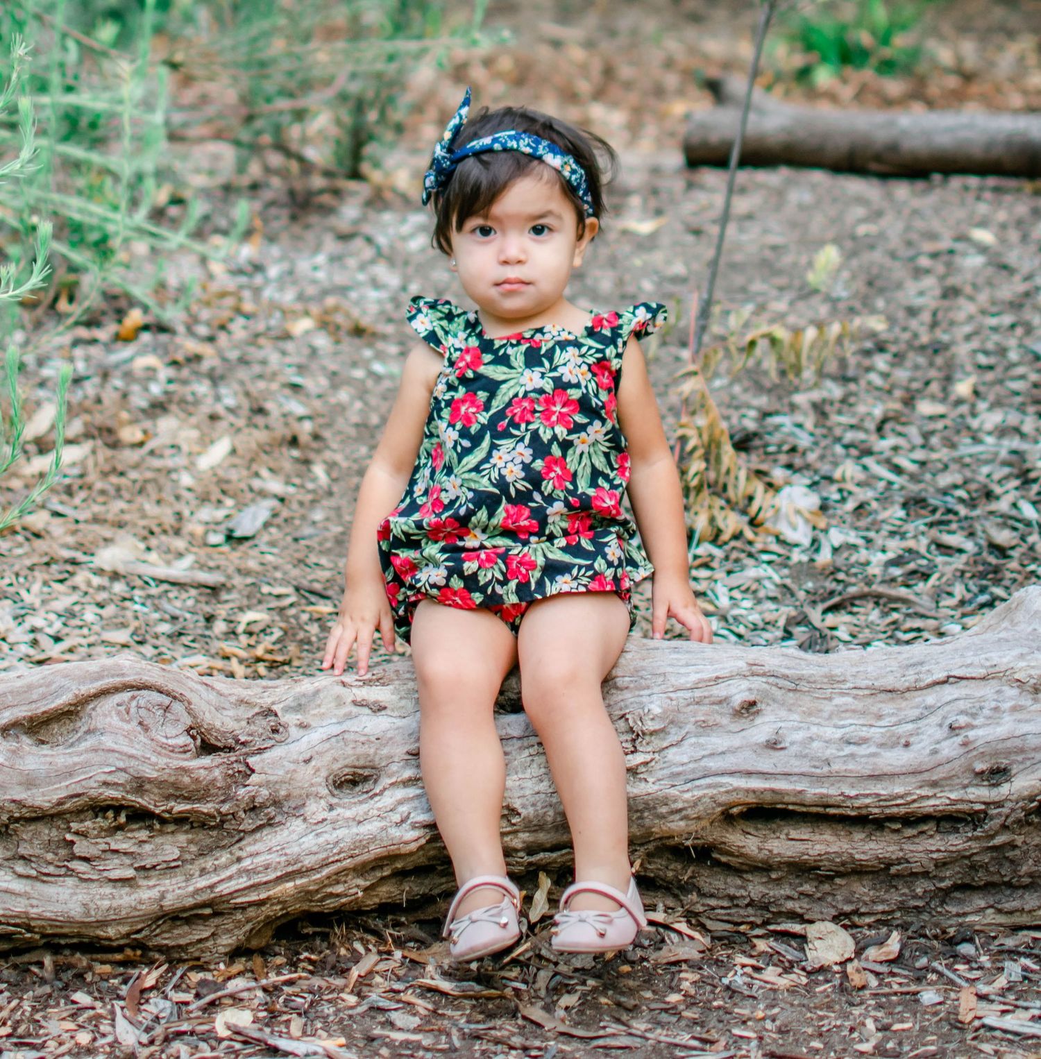 Photos on a fallen tree trunk in a wooded area showing a floral outfit and pink shoes.