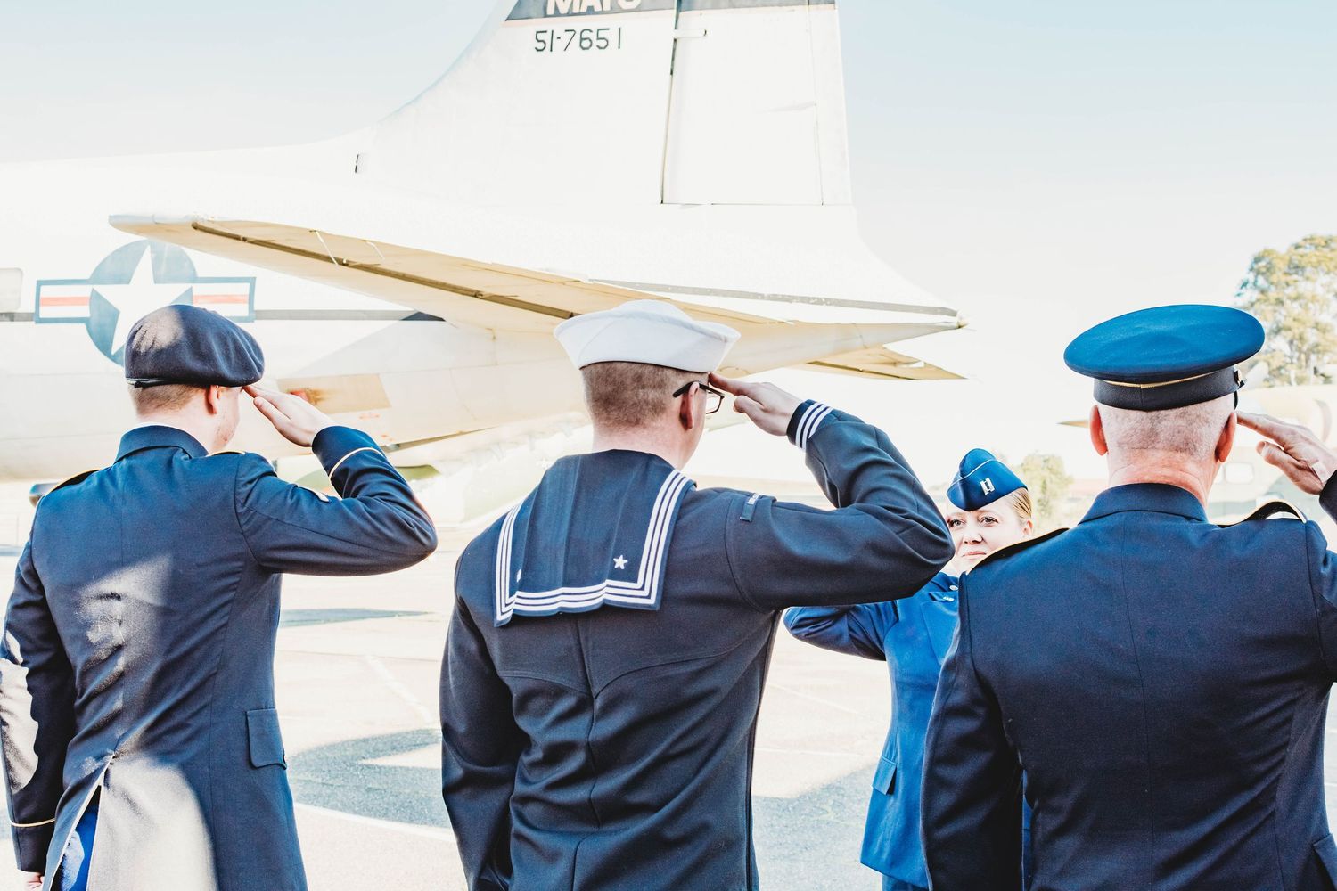Row of military service members in dress blues standing at attention beside an aircraft.