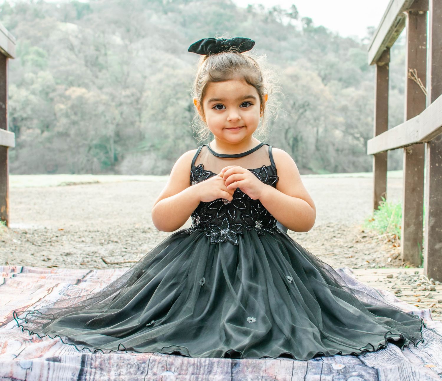 A young person in a flowing dark teal tulle dress poses on stone steps.