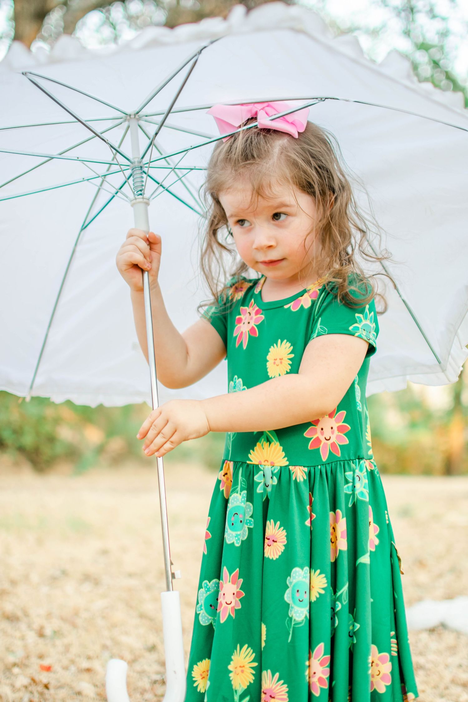 Playful poses with a clear umbrella wearing a green floral dress in a sunny outdoor setting.