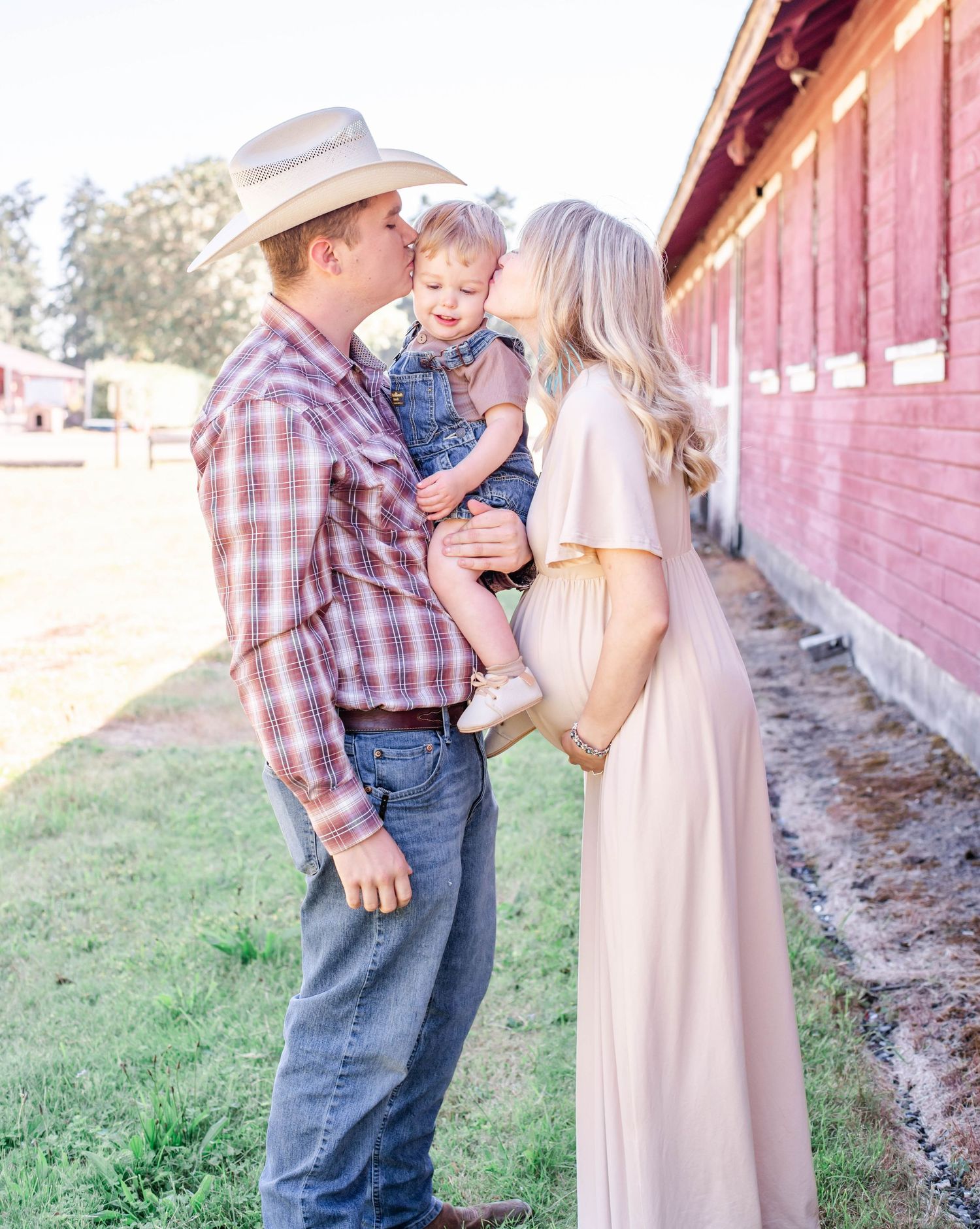 A family plays and laughs together during a summer photoshoot by a vintage red barn.