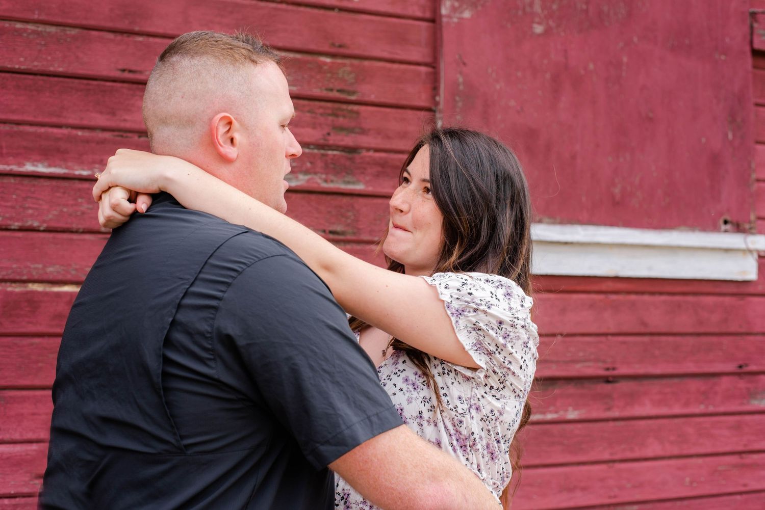 A couple shares an intimate moment against a red barn background during a photo session.