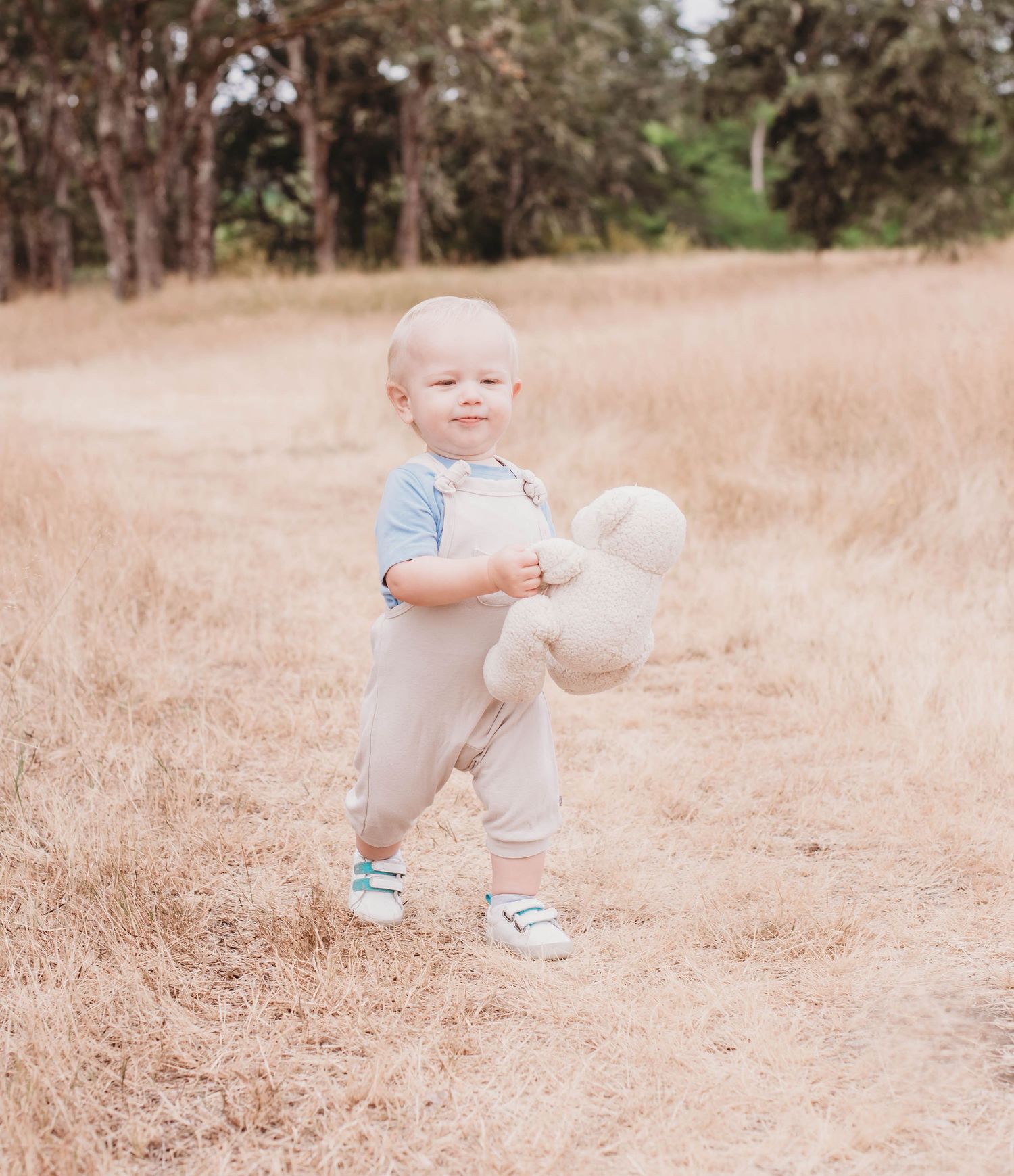 A small child playing in a sun-drenched field wearing blue and white clothing.
