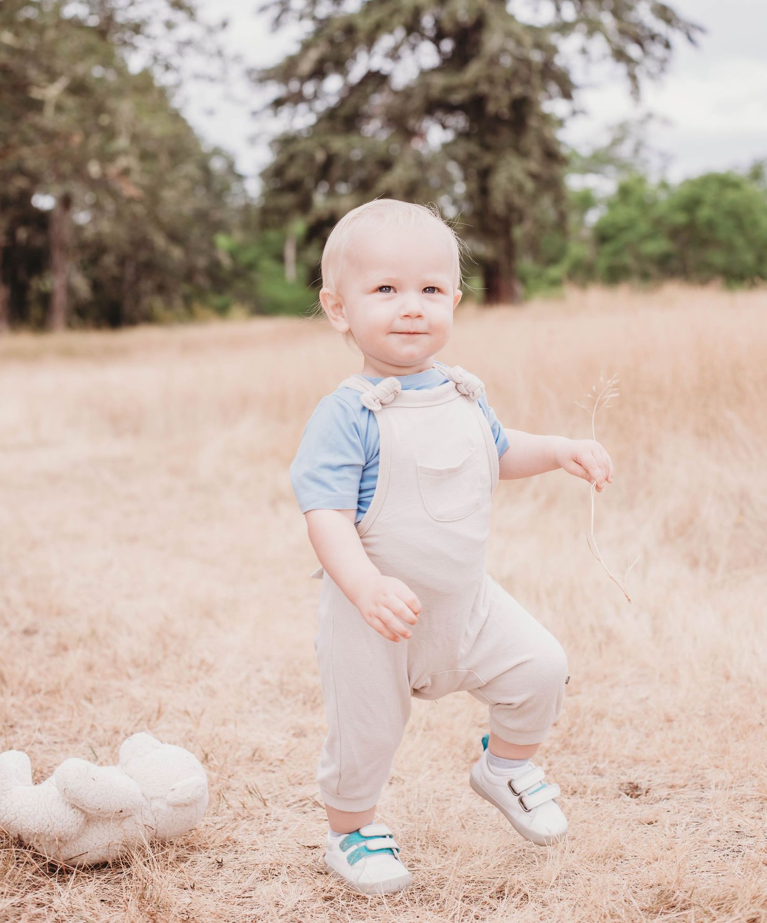 A toddler in casual wear playing in a natural outdoor setting with dried grass.