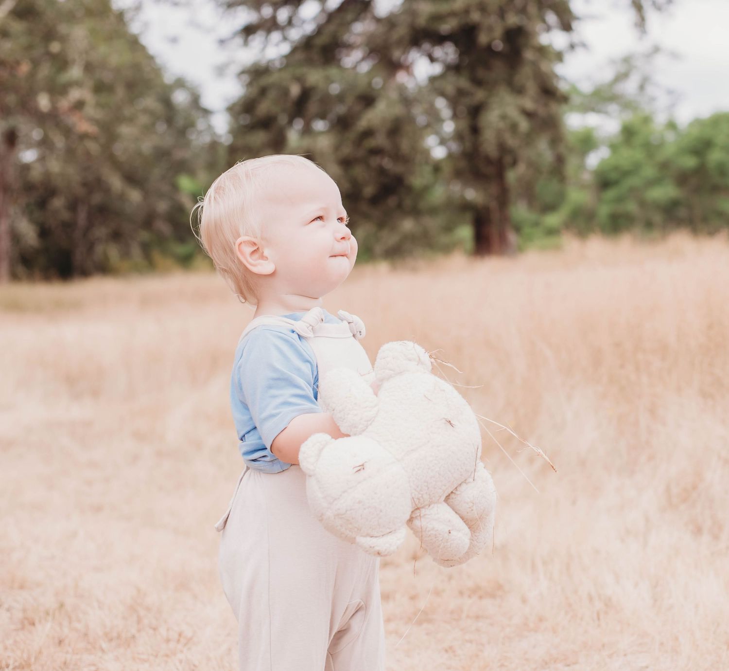 A young toddler exploring a sunlit meadow while holding a white toy.