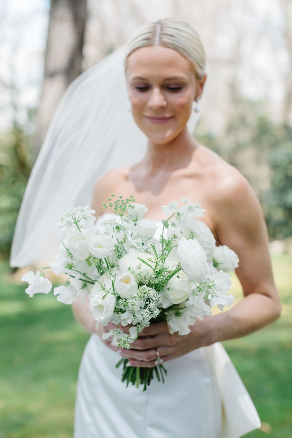 Beautiful white bridal bouquet with delicate flowers and baby's breath held against a classic strapless wedding gown.