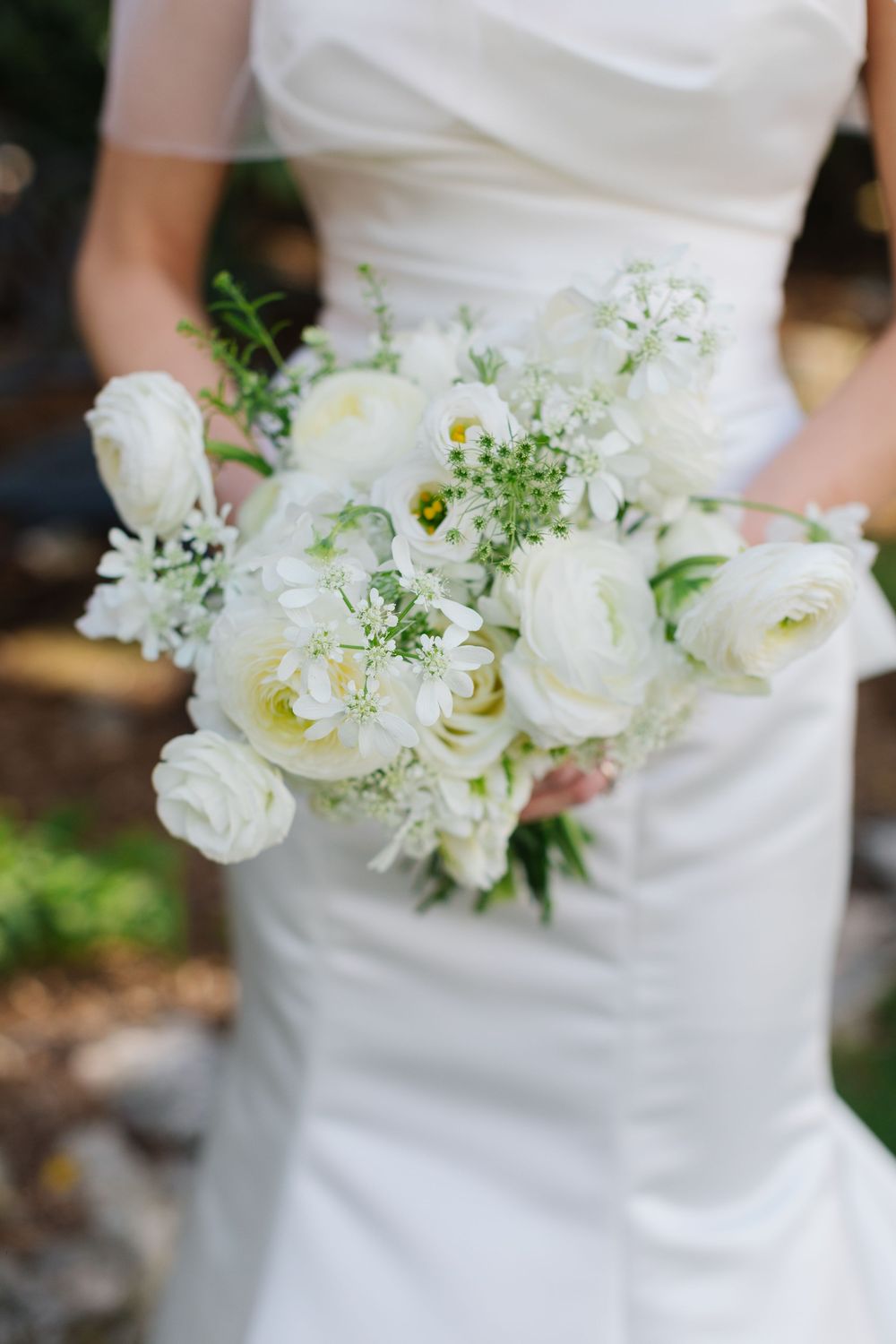 Close-up of elegant white wedding bouquet with roses and delicate greenery held against a white dress.