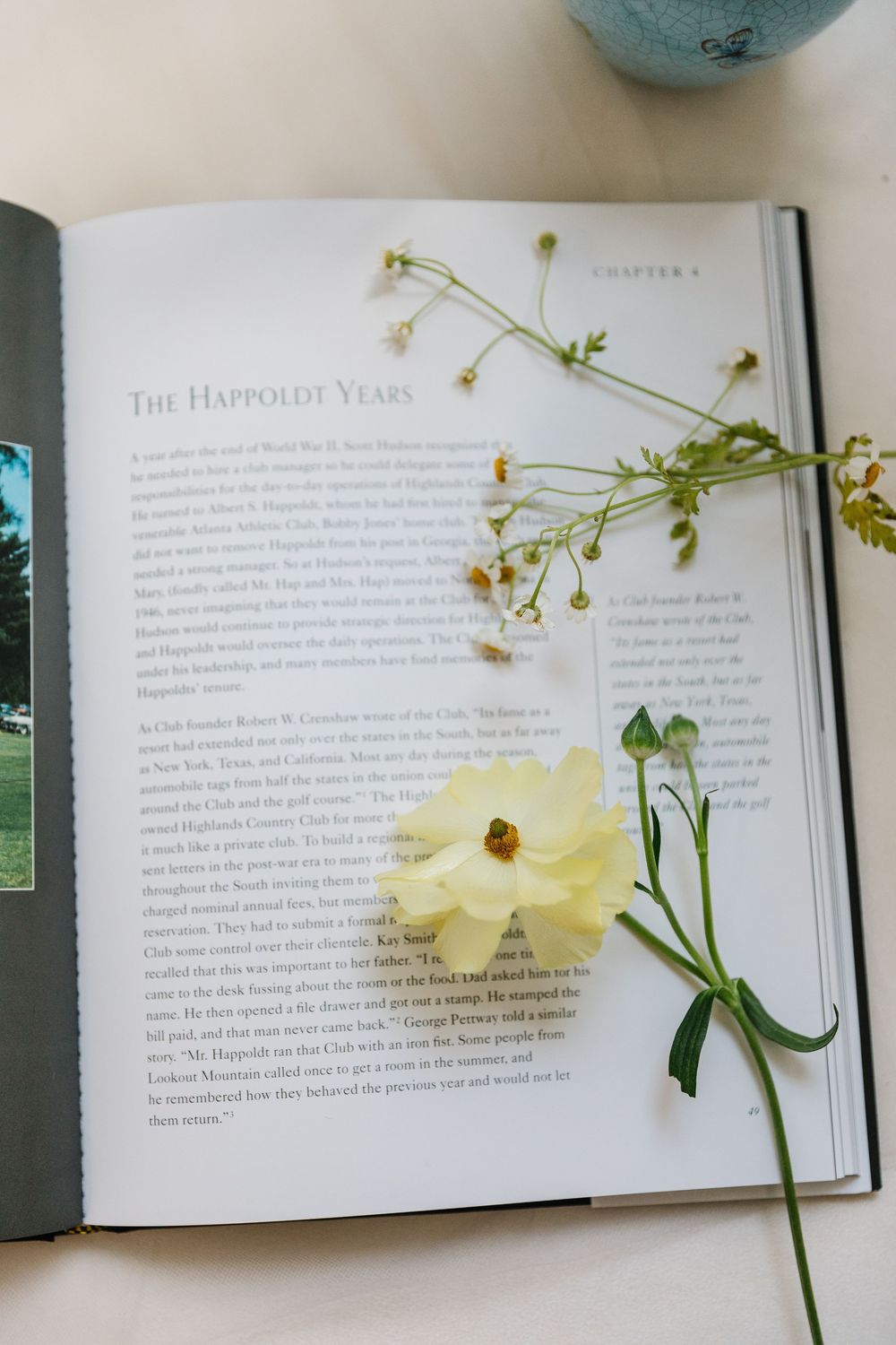 An open book page titled 'The Happiest Years' with a delicate yellow flower and wildflowers placed on top.