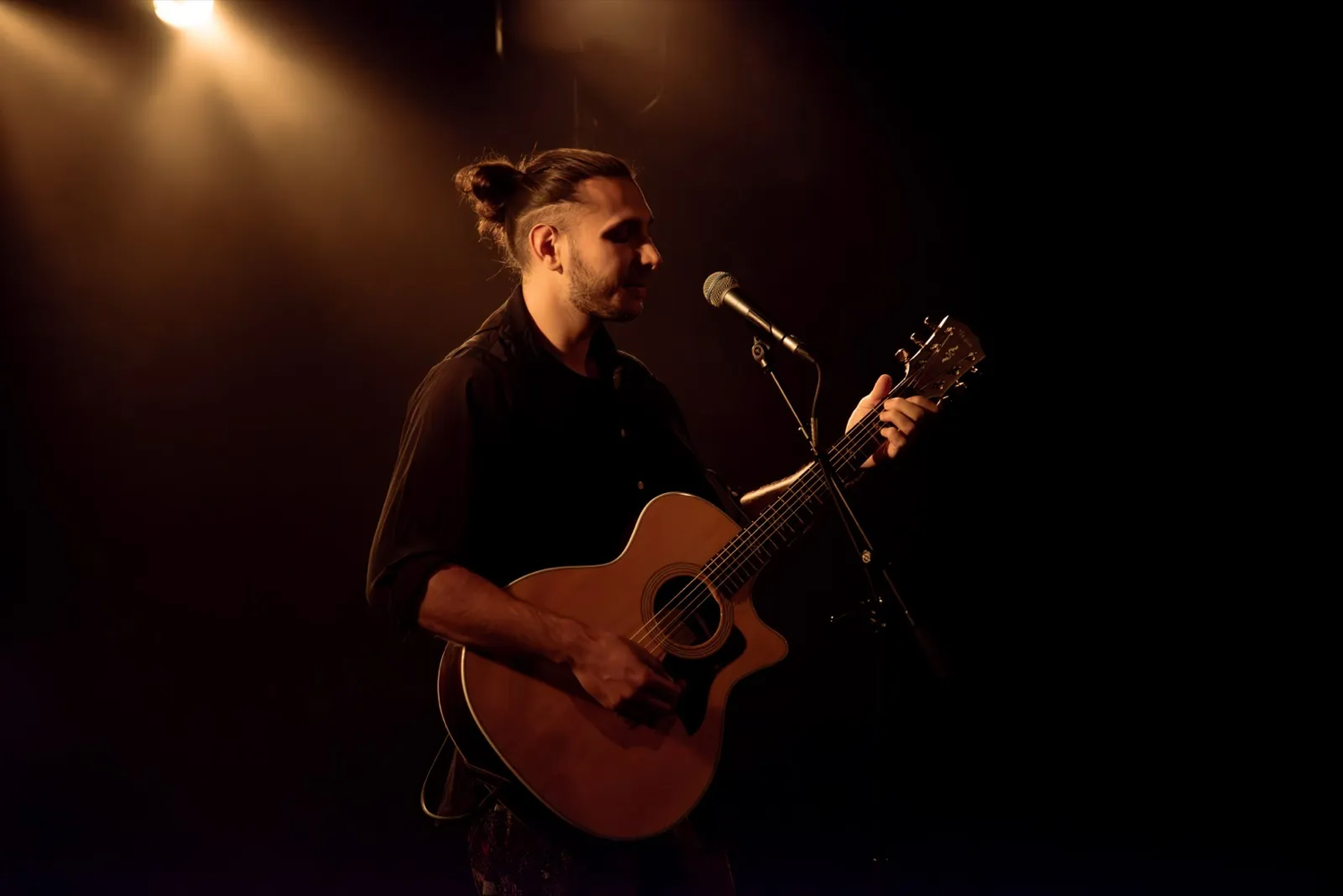 Musicien chantant et jouant de la guitare acoustique sur une scène sombre, éclairé par une lumière chaude.