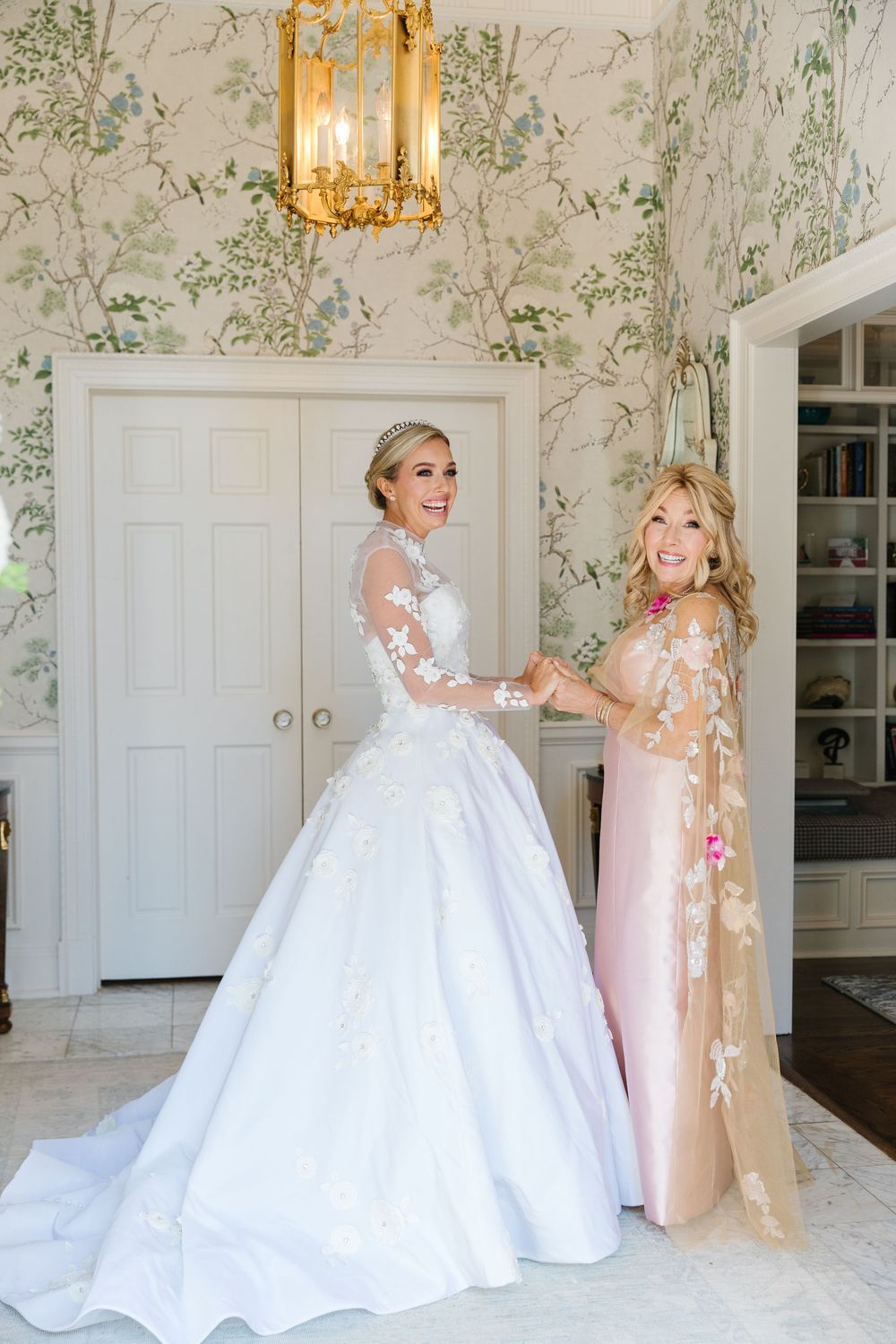Elegant bridal room interior with floral wallpaper, brass chandelier and white double doors serves as backdrop for wedding day.