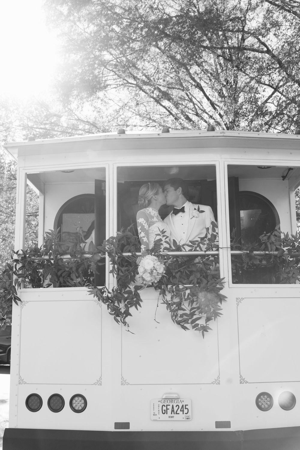 A black and white photo of a decorated vintage trolley or bus with floral arrangements in the windows.