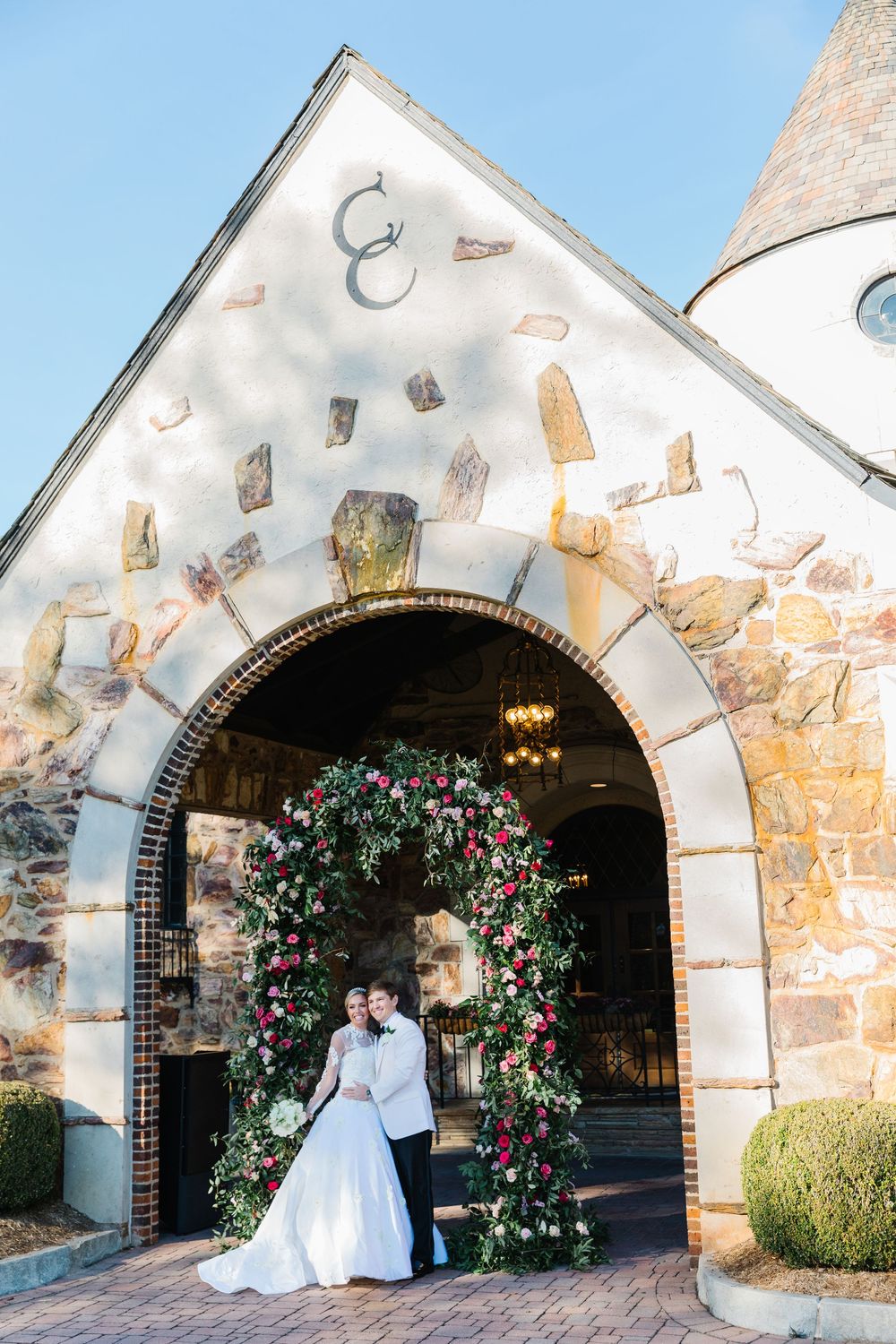 A romantic wedding venue entrance with stone archway decorated with a beautiful floral arch against a white castle-like facade.