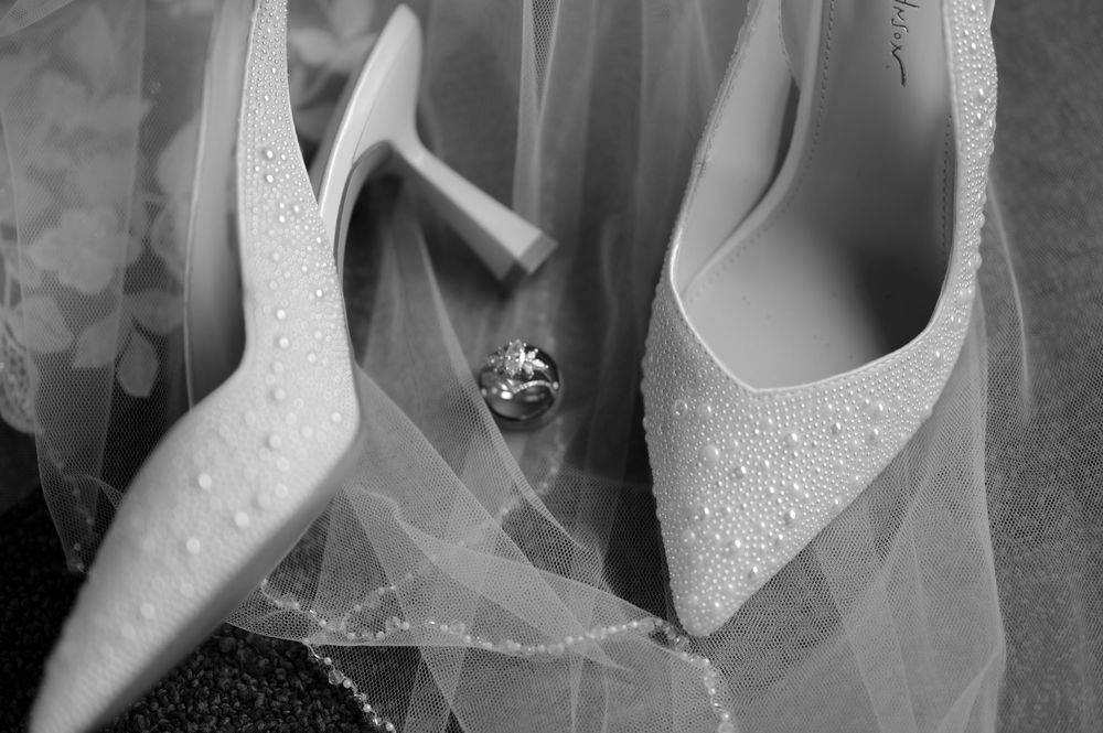 Black and white wedding photo of bridal shoes and engagement ring with delicate veil detail.