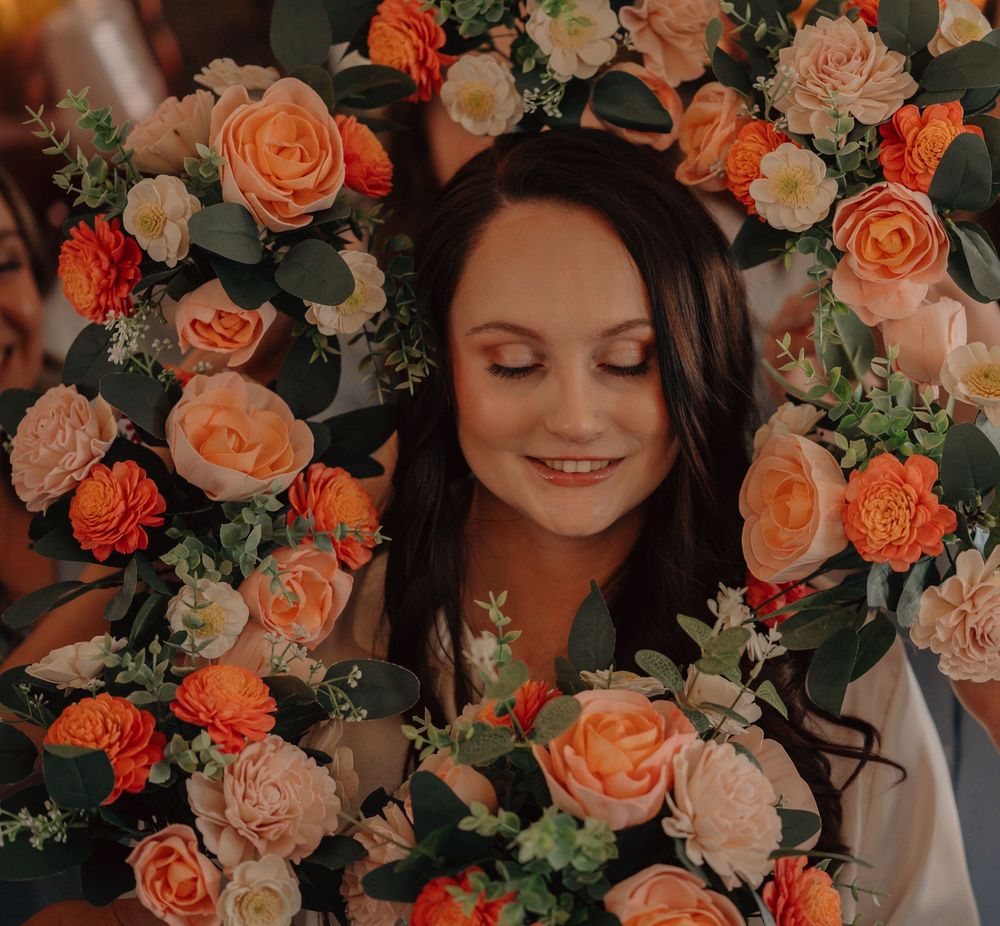 A serene smile amidst a backdrop of gorgeous coral and peach roses with lush greenery creating a romantic floral frame.