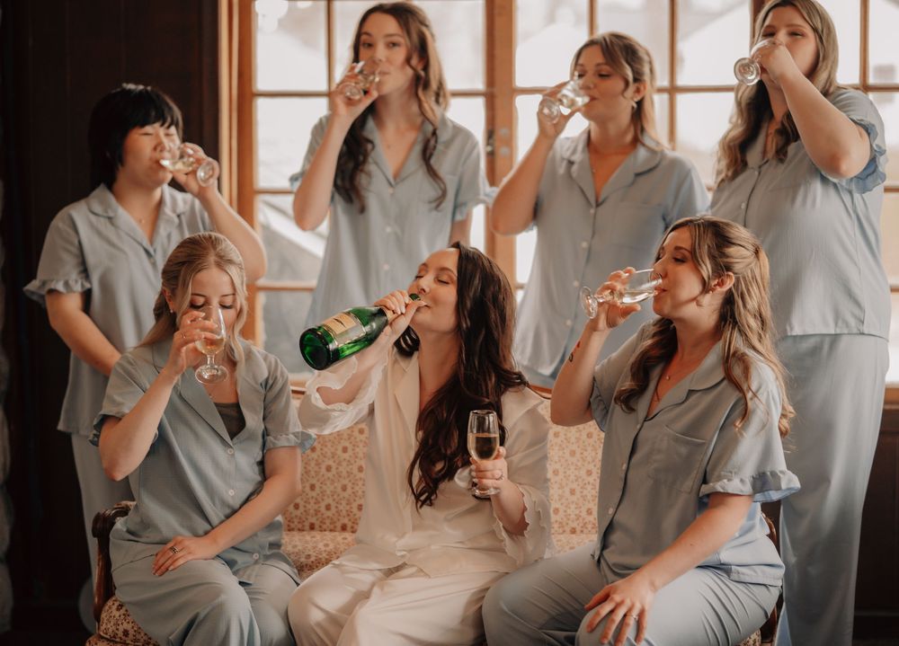 Group in matching gray pajamas celebrate with drinks and laughter during a casual indoor party.