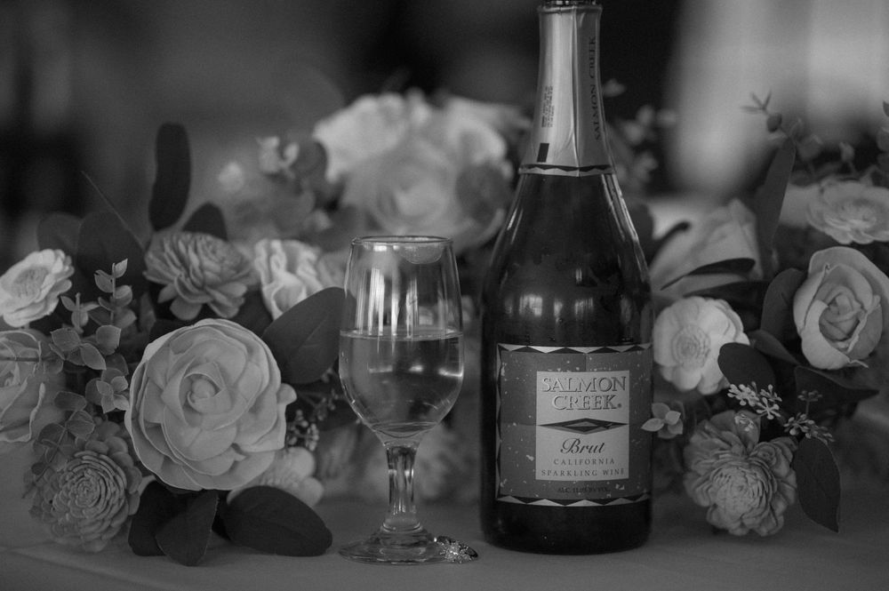 A black and white photograph of a wine bottle and glass surrounded by elegant roses on a table setting.