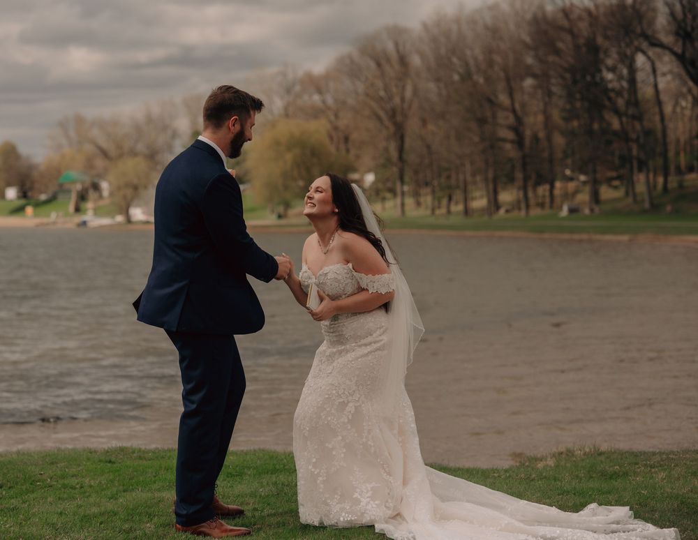 A wedding couple standing on a beach shore during an overcast day with trees in the background.